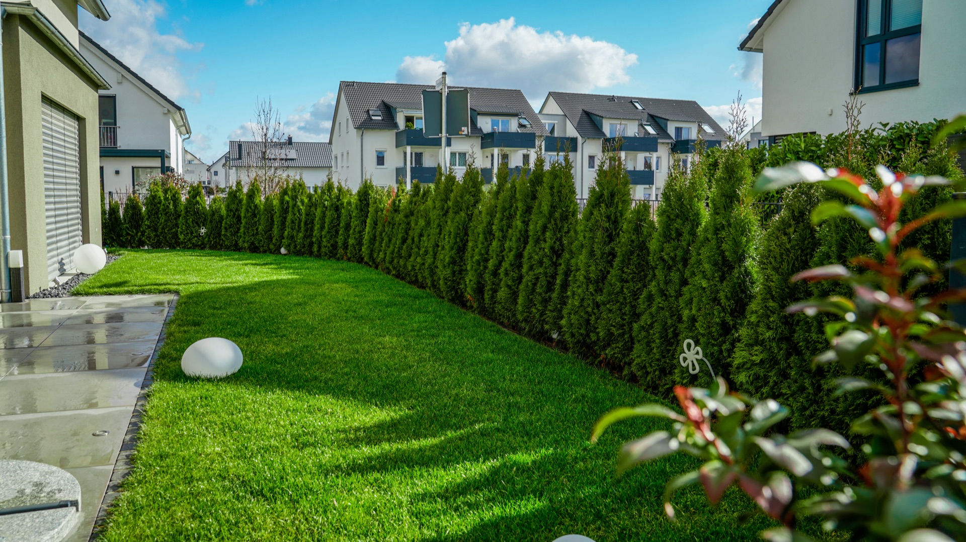 Garten in Benningen: Rasen, immergrüne Säulenhecke als Sichtschutz und eine Kugelleuchte
