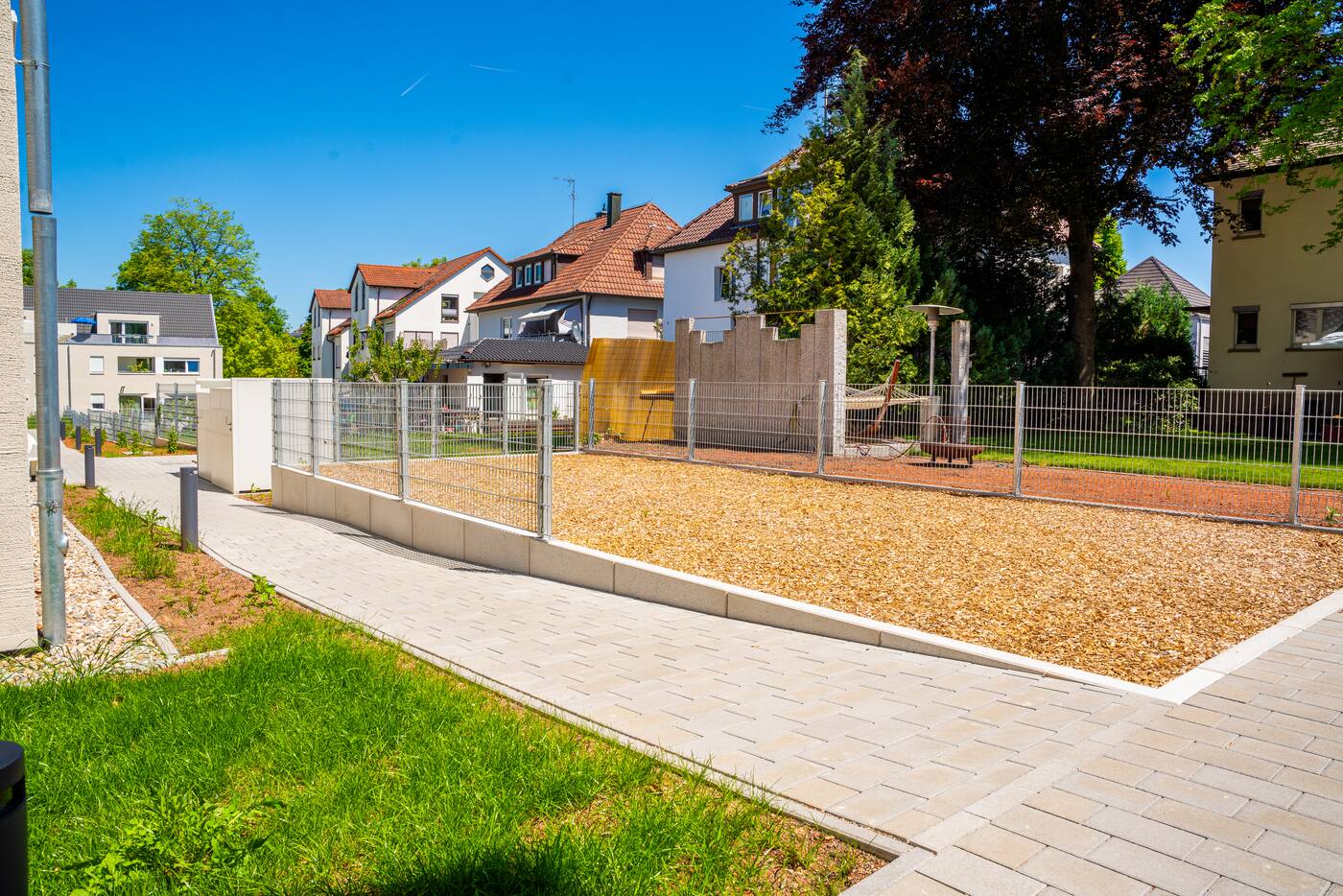 Außenanlagen einer Wohnanlage während der Arbeiten: gepflasterte Wege und Spielplatzfläche hinter dem Bauzaun